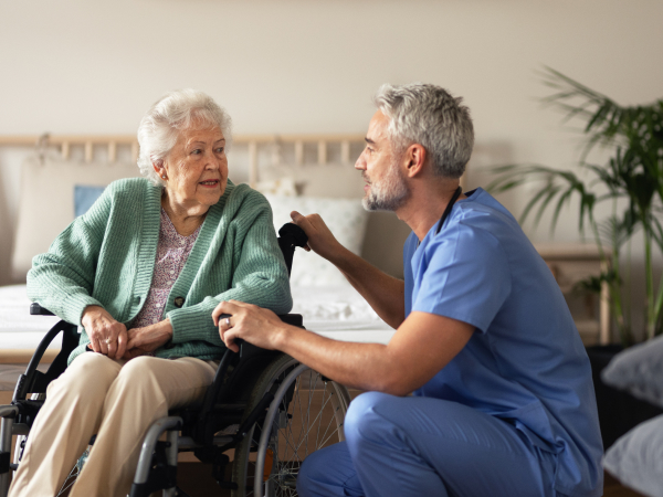 Männliche Pflegekraft spricht mit älterer Dame im Rollstuhl